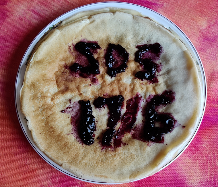 Une pile de crêpes avec écrit « ZDS 17/6 » au dessus avec de la confiture de myrtilles